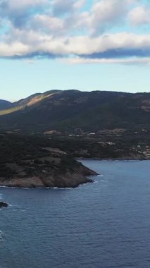 Korsika, Cargese yakınlarında gür tepeleri ve dramatik bulutları olan engebeli bir kıyı şeridi manzarası. Sakin mavi deniz, kayalık kıyı ve yeşil manzarayla çelişiyor..