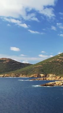 Delta du Fango 'daki engebeli kıyı şeridi ve açık mavi suların manzarası, yeşil tepeler ve parçalı bulutlu gökyüzü. Doğa, seyahat ve manzara kavramları için ideal..