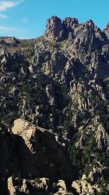 Fransa 'nın Korsika kentindeki açık mavi gökyüzünün altında Col de Bavella' nın engebeli uçurumları ve dramatik kayalıkları. Yamaçlara yayılmış çam ağaçları ile doğal manzara.