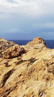 Yeşil kubbeli beyaz deniz feneri parçalı bulutlu bir gökyüzünün altında Fanale di Petra 'ya bakan engebeli kayalık kayalıklara tünemiş..