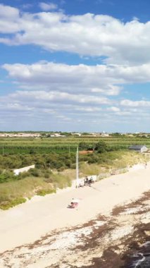 Geniş kumlu sahil, deniz yosunu, kum tepeleri ve Ile de Re, Fransa 'da parlak mavi bir gökyüzü altında dağınık ziyaretçiler. Kırsal alan ve arka planda küçük binalar.