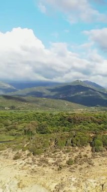 Delta du Fango 'nun yemyeşil, engebeli tepeleri ve Korsika' da parçalı bulutlu bir gökyüzünün altındaki uzak dağları manzarası..