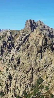 Korsika 'daki Col de Bavella' da açık mavi gökyüzünün altındaki dramatik kayalık dağ zirveleri. Nadir bitki örtüsü ve çarpıcı kayalıkları olan engebeli bir yer..