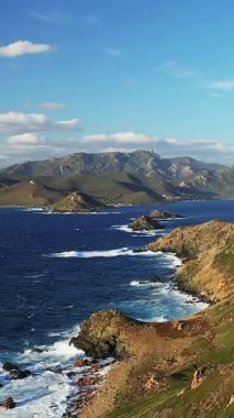 Sahile vuran dalgalarla dolu dramatik kayalık kıyı şeridi, Korsika 'daki Les Iles Sanguinaires' te mavi bir gökyüzünün altında. Engebeli arazi ve canlı deniz çarpıcı bir doğal manzara yaratır..