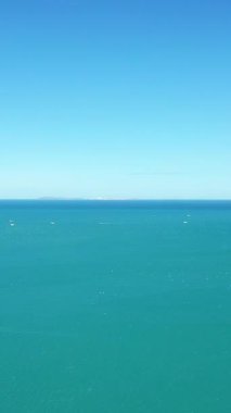 Açık mavi gökyüzünün altında engin bir turkuaz deniz, Isola Varano doğa rezervi yakınlarındaki ufukta görünen uzak tekneler. Sakin ve asgari kıyı manzarası.