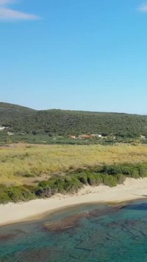 Yunanistan 'ın Gythio kenti yakınlarındaki kumlu sahil manzarası, yeşil bitki örtüsü ve dalgalı tepeler, açık mavi bir gökyüzü altında..