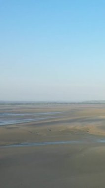Fransa 'nın Le Mont-Saint-Michel şehrinde açık mavi gökyüzünün altındaki geniş gelgit düzlükleri. Islak kum desenleri ve uzak ufuklarıyla sakin bir manzara..