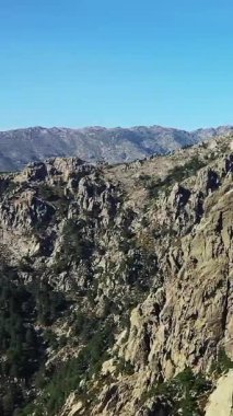 Korsika 'daki Col de Bavella' da açık mavi gökyüzünün altında dramatik kayalık tepeler ve engebeli arazi. Görkemli dağ manzarası doğa ve seyahat temaları için ideal.