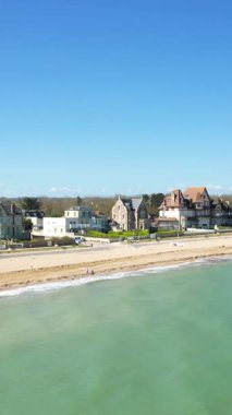 Lion-sur-Mer 'deki Kılıç Sahili manzaralı. Zarif sahil evleri, kumlu kıyılar ve berrak mavi gökyüzünün altında durgun turkuaz su..