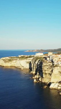 Korsika 'nın Bonifacio kentindeki engebeli beyaz kayalıkların ve açık gökyüzünün altındaki mavi Akdeniz' e bakan kıyı kasabasının havadan görünüşü..