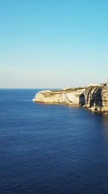 Bonifacio, Korsika 'da açık bir gökyüzünün altında, derin mavi Akdeniz' in üzerinde dramatik beyaz kireçtaşı kayalıkları yükseliyor. Kıyı manzarası doğal güneş ışığıyla yıkanır, sakin ve resimli bir manzara yaratır..