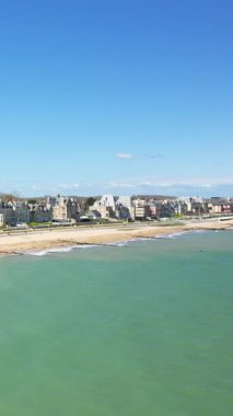 Sword Beach 'in manzarası ve Lion-sur-Mer, Normandiya, Fransa' daki deniz evleri, açık mavi gökyüzünün altında. Sakin dalgalar bu sakin sahil sahnesinde yavaşça kumlu kıyıya ulaşır..