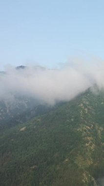 Ağaçlarla kaplı yemyeşil dağlar, alçak bulutlar Pireneler üzerinde sürükleniyor. Berrak mavi gökyüzünün altında sakin doğal manzara.