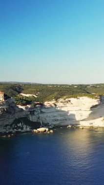 Bonifacio, Korsika 'da berrak mavi sulara bakan kıyı kasabası olan dramatik beyaz kireçtaşı uçurumları. Parlak güneş ışığı, engebeli Akdeniz manzarasını vurguluyor.