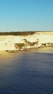 Bonifacio, Korsika 'da berrak bir gökyüzünün altında durgun mavi denizin üzerinde yükselen beyaz kireçtaşı kayalıkların manzarası. Sıcak güneş ışığıyla yıkanmış doğal kıyı manzarası..