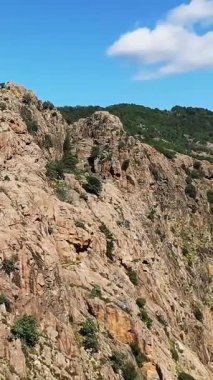 Korsika 'nın Vallee de Porto şehrinde engebeli kayalık uçurumların ve mavi gökyüzünün altındaki yeşil tepelerin manzarası. Parlak gün ışığı doğal manzarayı vurgular.