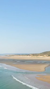 Fransa 'nın Plage de la Vieille Eglise şehrinde açık mavi gökyüzü altında yumuşak dalgalar ve çimenli kumullarla geniş kumlu bir sahil. Huzurlu kıyı manzarası seyahat ve doğa kavramları için ideal..