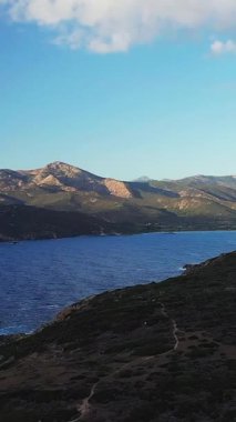 Korsika, Cargese yakınlarında açık mavi bir gökyüzünün altında engebeli kıyı şeridi ve deniz kıyısının manzarası. Dramatik arazi ve sakin suyla doğal Akdeniz manzarası.