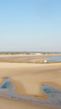 Fransa 'nın Plage de la Potiniere şehrinde gelgit havuzları ve açık mavi gökyüzü olan geniş kumlu bir sahil. Seyahat ve doğa kavramları için ideal sakin kıyı sahnesi.