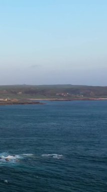 Fransa 'nın Normandiya, Cap de la Hague kentindeki engebeli kıyı şeridi ve sakin deniz manzarası. Yumuşak dalgalar, arka planda yeşil tepelerle kayalık kıyılara vurur..