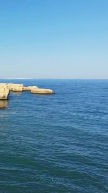 Temiz mavi okyanus suyu ve Albufeira, Portekiz yakınlarındaki Algarve kıyı şeridi boyunca uzanan engebeli kireçtaşı kayalıkları parlak bir gökyüzünün altında..