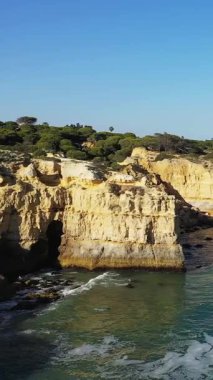 Portekiz, Albufeira yakınlarındaki Algarve kıyısında dramatik altın tepeler ve berrak mavi bir gökyüzü. Bereketli yeşil bitki örtüsü huzurlu denizin üzerindeki engebeli kıyı şeridini taçlandırıyor..
