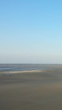 Fransa 'nın Le Mont-Saint-Michel yakınlarında açık mavi bir gökyüzünün altındaki kumlu gelgit düzlüklerinin geniş manzarası. Sakin atmosferi olan minimalist bir manzara..