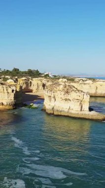 Portekiz, Albufeira yakınlarındaki Algarve kıyı şeridi boyunca uzanan engebeli kireçtaşı kayalıkları ve deniz mağaralarının manzarası, berrak mavi gökyüzü ve turkuaz suyuyla.
