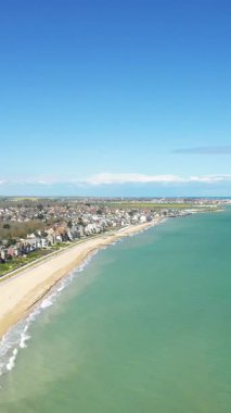 Sword Beach 'in manzaralı manzarası ve Hermanville-sur-Mer' in kıyı şeridi turkuaz su ve açık mavi gökyüzünün altında kıyı boyunca evler..