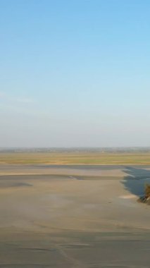 Fransa 'nın Le Mont-Saint-Michel yakınlarında açık mavi bir gökyüzünün altındaki kumlu gelgit düzlüklerinin geniş manzarası. Yumuşak ışık ve açık alanla doğal manzara.