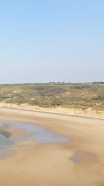 Fransa, Plage de la Vieille Eglise 'de açık mavi gökyüzü altında gelgit havuzları ve çimenli kumulları olan geniş kumlu bir sahil. Sakin kıyı manzarası doğa ve seyahat kavramları için idealdir..