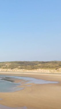 Fransa 'nın Plage de la Vieille Eglise şehrinde açık mavi gökyüzünün altında gelgit havuzları ve çimenli kumulları olan geniş kumlu bir sahil..