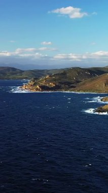 Korsika, Les Iles Sanguinaires 'teki engebeli kıyı şeridinin ve derin mavi denizin manzarası, dağınık bulutlarla dolu parlak bir gökyüzünün altında..