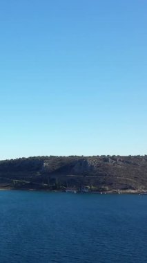 Yunanistan 'ın Nauplie kenti yakınlarındaki Paralia Karathona sahilindeki kayalık kıyı şeridi ve berrak mavi suları bulutsuz bir gökyüzünün altında geniş bir manzara. Huzurlu Akdeniz manzarası seyahat ve doğa kavramları için ideal.