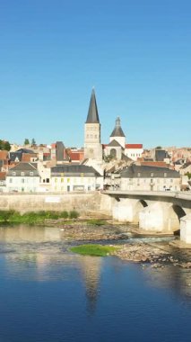 La Charite-sur-Loire manzarası. İkonik kilise kuleleri, geleneksel binaları ve Loire Nehri üzerindeki taş köprüsü berrak mavi gökyüzünün altında..