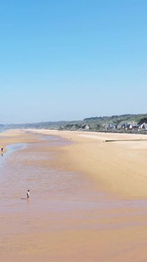 Geniş kumlu plaj alçak gelgitte uzak evler ve açık mavi gökyüzü Omaha Sahili, Normandiya, Fransa.