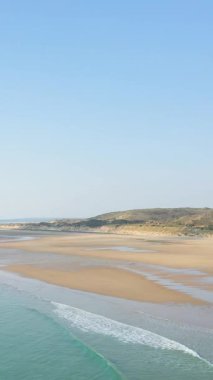 Plage de la Vieille Eglise 'in sakin bir görüntüsü. Yumuşak dalgalar, geniş kum ve açık mavi gökyüzü altında çimenli kum tepeleri. Doğa kavramları, rahatlama ve kıyı manzaraları için ideal..