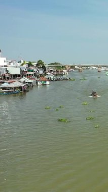 Vietnam, Chau Doc nehri boyunca yüzen bir köyün manzarası, açık mavi gökyüzünün altında tekneler, stilt evler ve su tesisleri var..