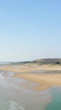Geniş kumlu kıyı şeridinin ve Plage de la Vieille Eglise 'deki hafif dalgaların havadan görünüşü, berrak mavi gökyüzünün altındaki uzak tepeler..