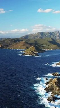 Parlak bir gökyüzünün altında, Les Iles Sanguinaires, Korsika 'da dramatik kayalık kıyı şeridi ve derin mavi deniz. Kıyıya vuran engebeli arazi ve dalgalar çarpıcı bir doğal manzara yaratır..