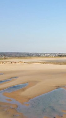 Fransa 'nın Plage de la Potiniere şehrinde açık mavi gökyüzünün altında sığ su havuzları olan geniş kumlu bir sahil. Sakin ve huzurlu kıyı manzarası ufukta görünen uzak bir kasaba..