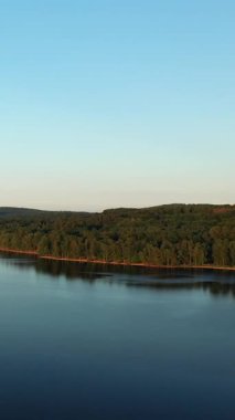 Fransa 'nın Settons Gölü' nde, açık bir akşam gökyüzünün altında sık yeşil ormanlarla çevrili sakin bir göl. Huzurlu su ve gür ağaçlarla huzurlu doğal manzara.