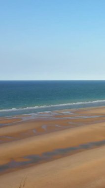 Fransa, Normandiya 'da açık mavi gökyüzü altında altın kum ve yumuşak dalgalarla geniş bir Omaha Sahili manzarası.