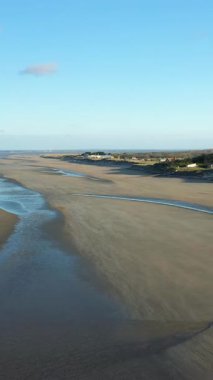 Geniş kumlu kıyı şeridi. Narin dalgalar ve açık mavi gökyüzü altında uzak evler. Utah Sahili, Normandiya, Fransa. Huzurlu kıyı manzarası seyahat ve doğa kavramları için ideal..