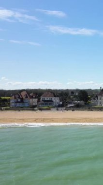 Hermanville-sur-Mer 'deki Kılıç Sahili' nin güneşli manzarasında sakin dalgalar, kumlu kıyılar ve açık mavi gökyüzü altında kıyı evleri var..