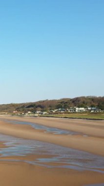 Islak kum desenli geniş bir Omaha Sahili manzarası ve Fransa 'nın Normandiya şehrinde açık mavi gökyüzünün altında küçük bir kıyı köyü..