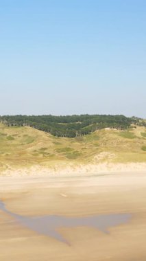 Plage de la Vieille Eglise 'de kumsalın geniş manzarası, kayan kumullar ve açık mavi gökyüzünün altında bir orman alanı. Doğal kıyı manzarası arka planlar veya seyahat kavramları için idealdir..
