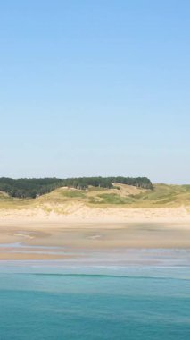 Plage de la Vieille Eglise 'de berrak bir gökyüzü altında kumlu sahil, kıyı kum tepeleri ve açık mavi deniz manzarası..
