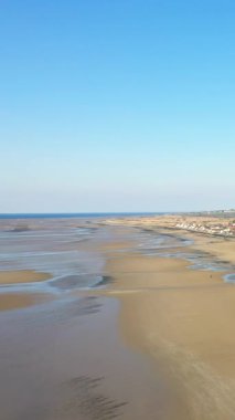 Asnelles, Fransa 'daki Gold Beach' in geniş manzarası açık mavi gökyüzünün altındaki ıslak kum ve gelgit havuzlarını gösteriyor. Uzak kıyı şeridi ve sakin denizi olan sakin kıyı manzarası.