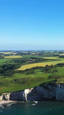 Fransa 'nın Etretat yakınlarındaki açık mavi gökyüzü altında dramatik beyaz uçurumlar, yeşil alanlar ve kıyı şeridi..
